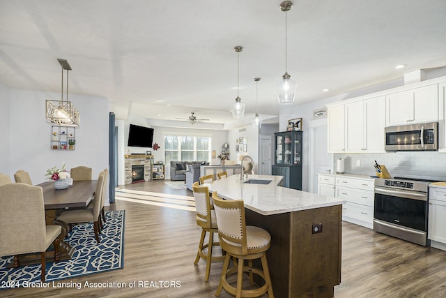 kitchen featuring ceiling fan, hanging light fixtures, a center island with sink, white cabinets, and appliances with stainless steel finishes