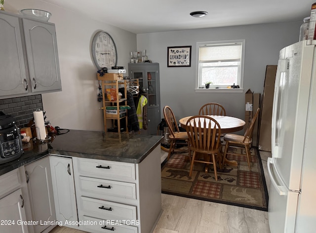 kitchen with backsplash, white cabinetry, white fridge, and light wood-type flooring