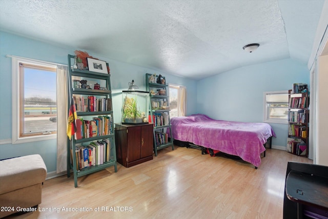 bedroom featuring a textured ceiling, light wood-type flooring, and vaulted ceiling