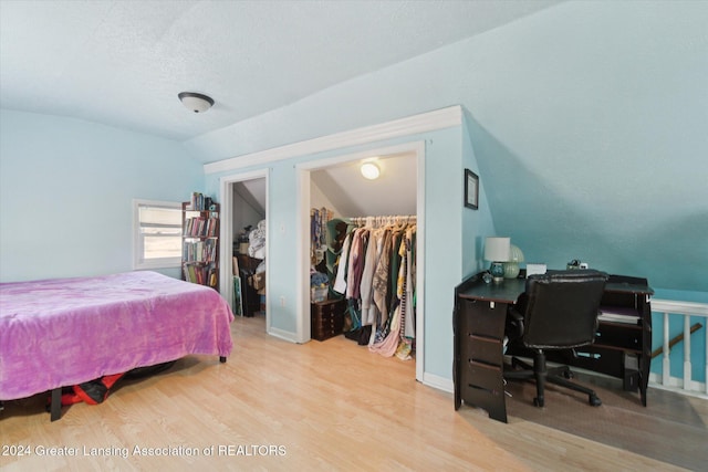 bedroom with a textured ceiling, lofted ceiling, light wood-type flooring, a closet, and a walk in closet