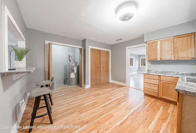 kitchen with sink, water heater, a textured ceiling, light brown cabinetry, and light wood-type flooring