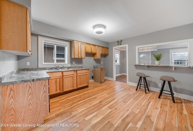 kitchen with a kitchen bar, a textured ceiling, light hardwood / wood-style flooring, and sink