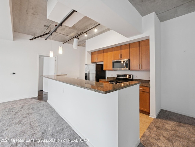 kitchen featuring dark stone counters, rail lighting, hanging light fixtures, appliances with stainless steel finishes, and light colored carpet