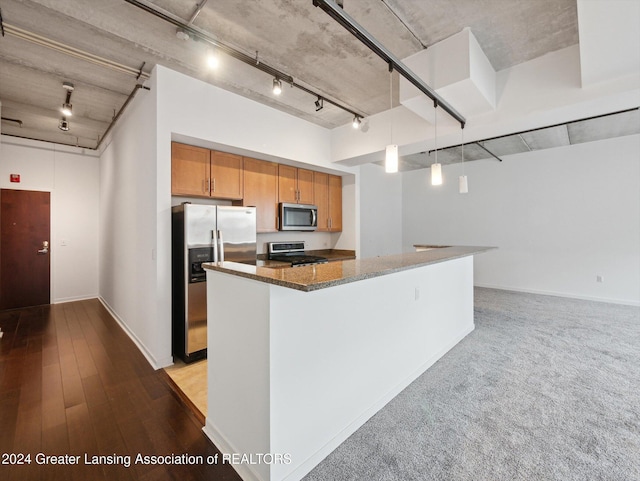 kitchen featuring stainless steel appliances, dark stone countertops, track lighting, decorative light fixtures, and light carpet