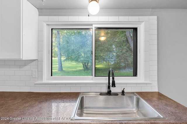 room details with white cabinets, backsplash, crown molding, and sink