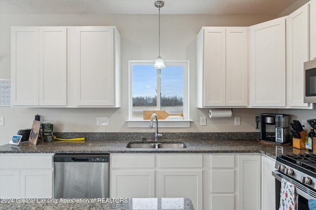 kitchen featuring appliances with stainless steel finishes, dark stone counters, sink, decorative light fixtures, and white cabinetry