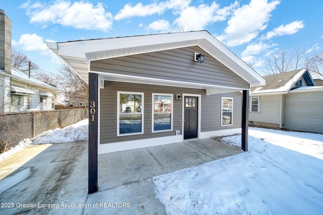 snow covered property with covered porch and fence