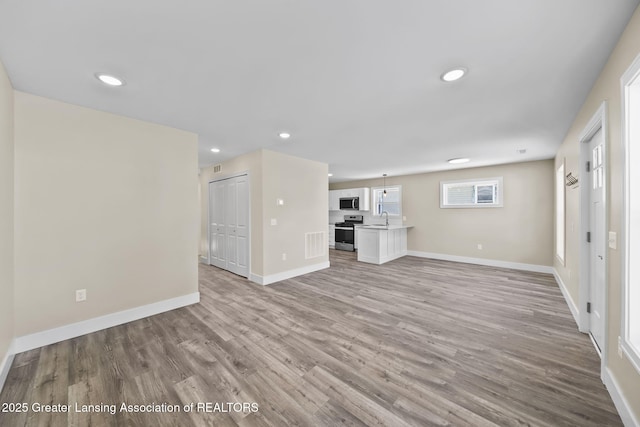 unfurnished living room featuring recessed lighting, baseboards, light wood finished floors, and a sink