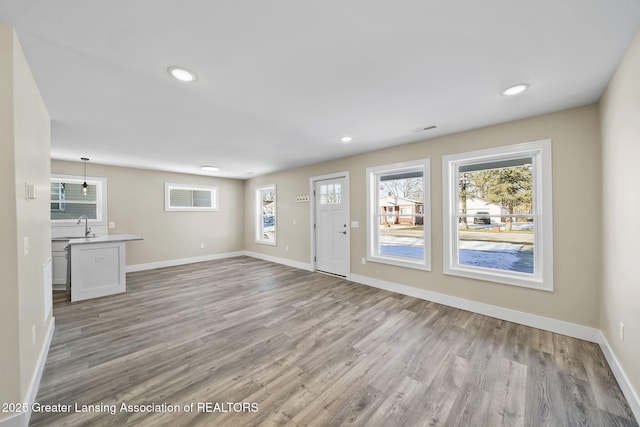 unfurnished living room with recessed lighting, light wood-type flooring, baseboards, and a sink