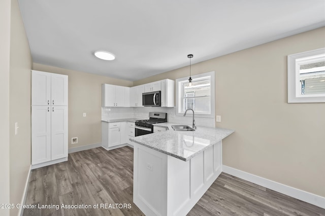 kitchen featuring a sink, light stone counters, white cabinetry, a peninsula, and gas range