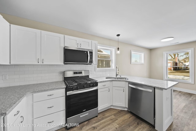 kitchen featuring a sink, dark wood-style floors, stainless steel appliances, a peninsula, and white cabinets