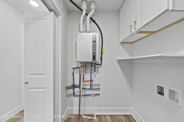 clothes washing area with water heater, cabinet space, baseboards, and wood finished floors