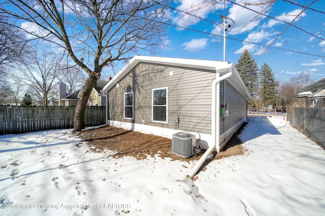 snow covered property with cooling unit and fence