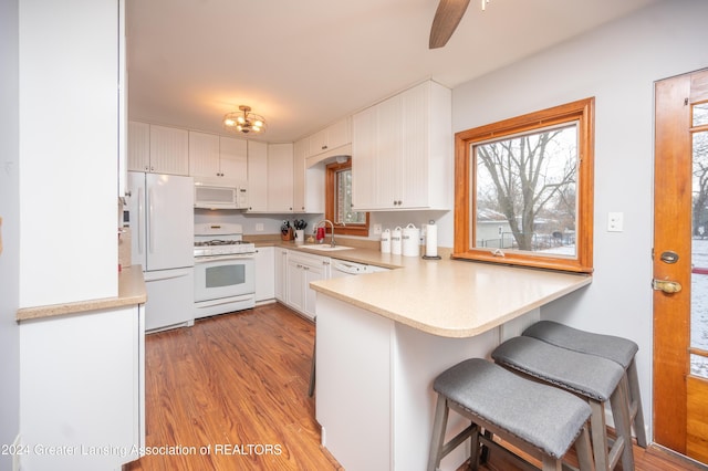 kitchen featuring white appliances, sink, light hardwood / wood-style floors, white cabinetry, and a breakfast bar area