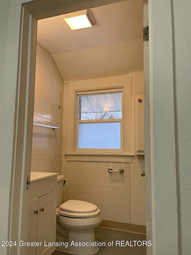 bathroom featuring tile walls, vanity, vaulted ceiling, and toilet