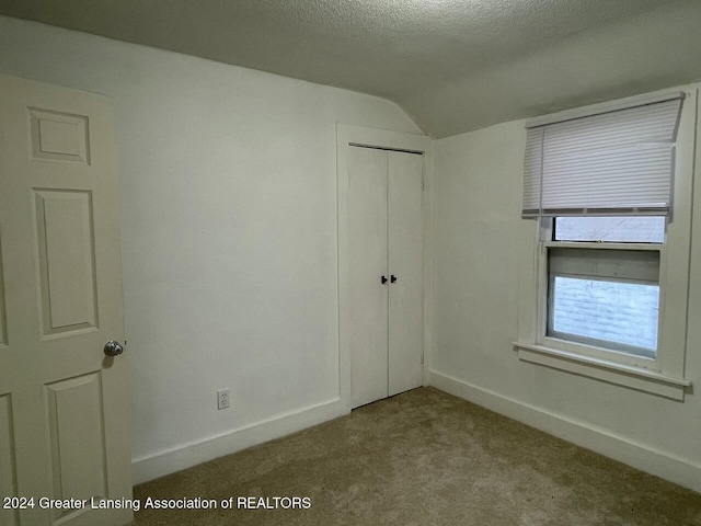 unfurnished bedroom with a closet, light colored carpet, a textured ceiling, and vaulted ceiling