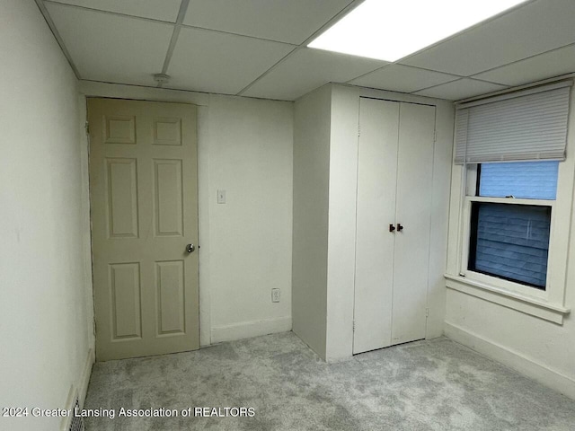 unfurnished bedroom with a paneled ceiling, light carpet, and a closet