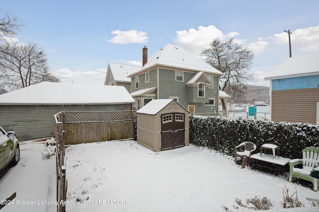 snow covered back of property featuring a storage shed