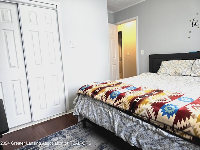 bedroom featuring dark wood-type flooring, crown molding, and a closet