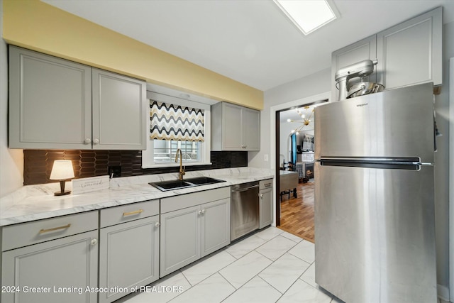 kitchen featuring light stone countertops, sink, tasteful backsplash, gray cabinets, and appliances with stainless steel finishes