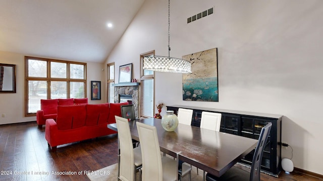 dining space with a stone fireplace, high vaulted ceiling, and dark hardwood / wood-style floors