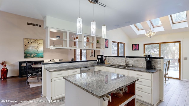 kitchen with lofted ceiling with skylight, dark stone countertops, white cabinets, and kitchen peninsula