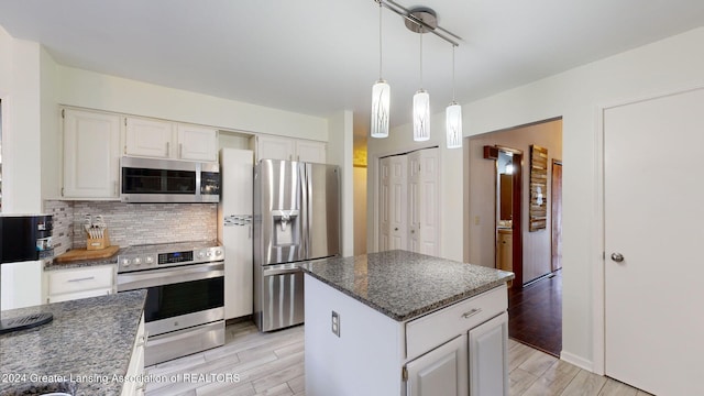 kitchen with a kitchen island, appliances with stainless steel finishes, decorative light fixtures, white cabinets, and backsplash