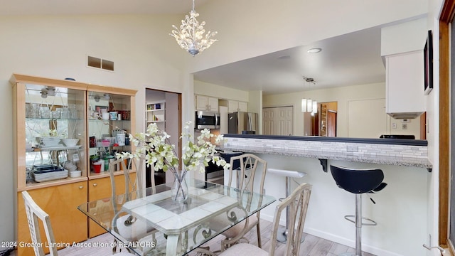 dining space with high vaulted ceiling, a chandelier, and light hardwood / wood-style flooring