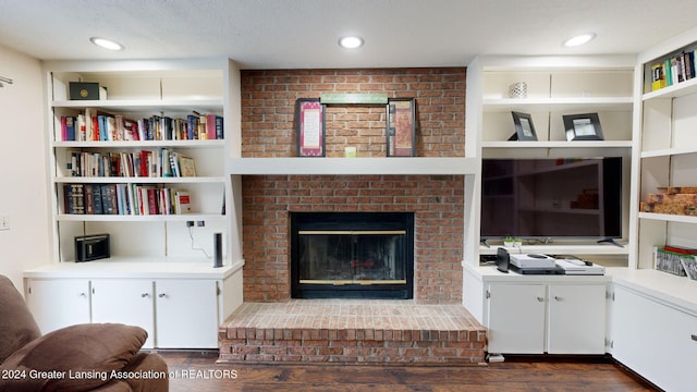 living room with a brick fireplace, dark wood-type flooring, and built in features