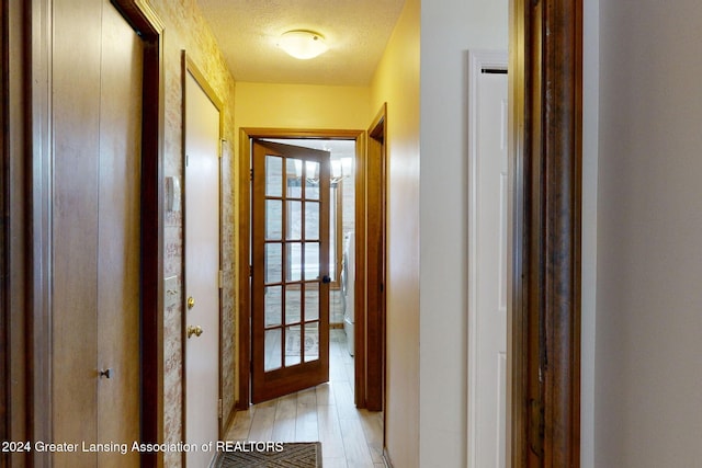 corridor with a textured ceiling and light wood-type flooring