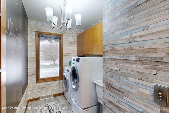 laundry room with cabinets, washing machine and clothes dryer, an inviting chandelier, and light hardwood / wood-style flooring