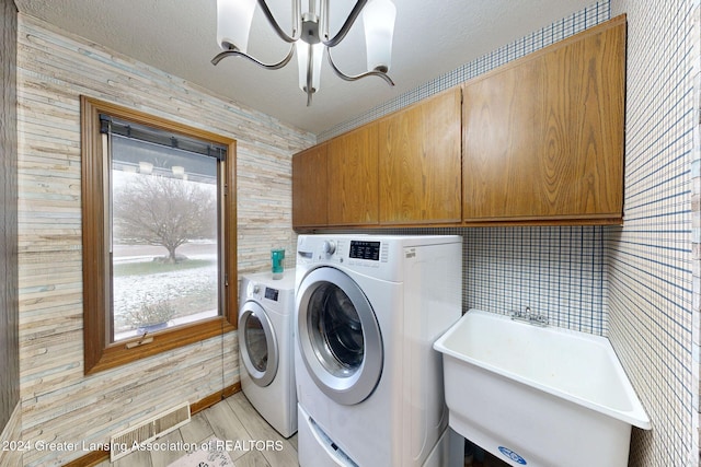 washroom featuring sink, light hardwood / wood-style flooring, cabinets, independent washer and dryer, and a textured ceiling