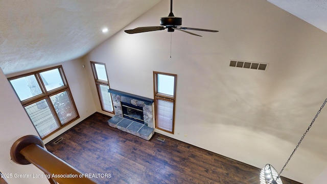 unfurnished living room featuring a stone fireplace, high vaulted ceiling, ceiling fan, dark wood-type flooring, and a textured ceiling