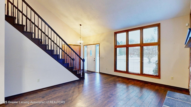 entryway with high vaulted ceiling, an inviting chandelier, and dark hardwood / wood-style flooring