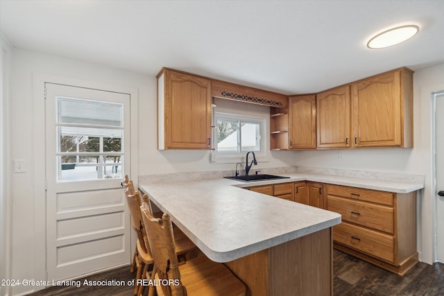 kitchen with sink, dark hardwood / wood-style flooring, a kitchen bar, and kitchen peninsula