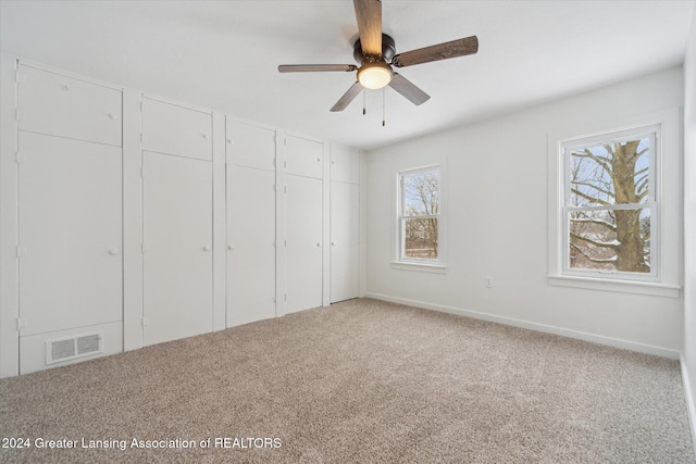 unfurnished bedroom featuring multiple closets, ceiling fan, multiple windows, and carpet flooring