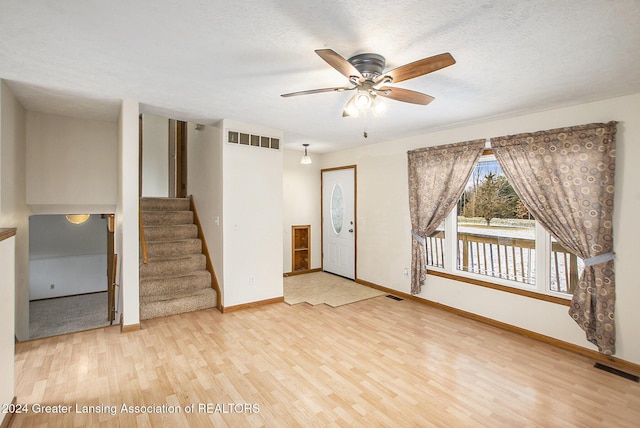 empty room with ceiling fan, light wood-type flooring, and a textured ceiling