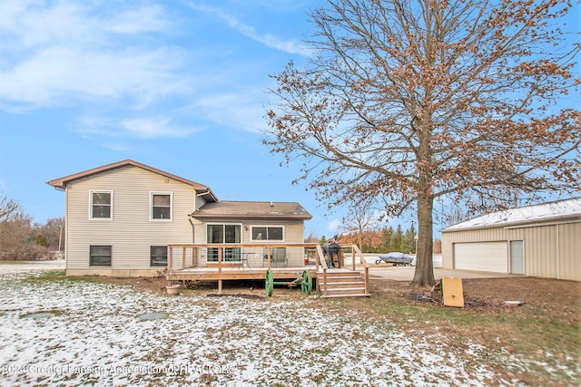 snow covered house featuring a wooden deck, an outbuilding, and a garage