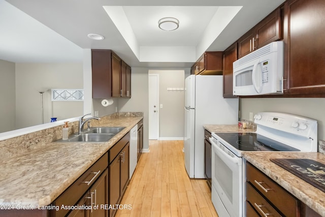 kitchen with white appliances, sink, a tray ceiling, and light hardwood / wood-style flooring