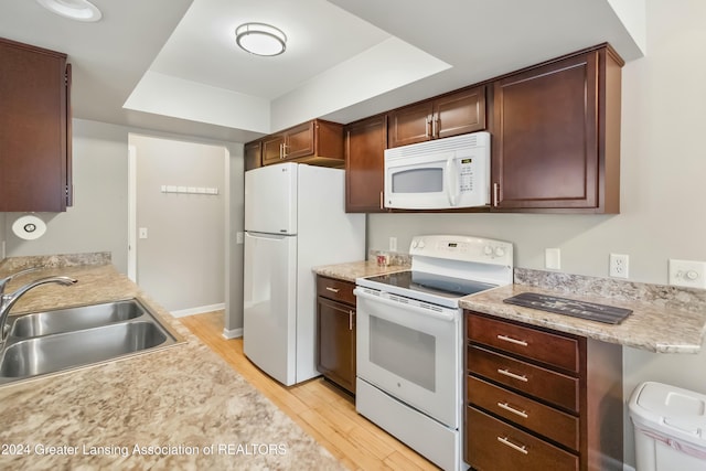 kitchen featuring a tray ceiling, sink, white appliances, and light wood-type flooring