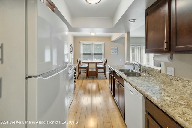 kitchen with dark brown cabinetry, sink, white appliances, and light wood-type flooring