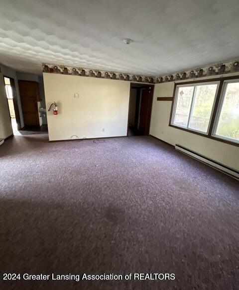 carpeted spare room with a textured ceiling and a baseboard heating unit