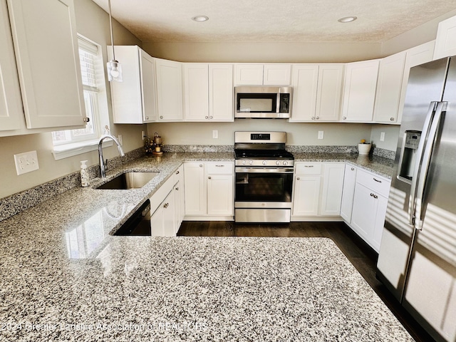 kitchen featuring stainless steel appliances, sink, white cabinets, light stone counters, and hanging light fixtures