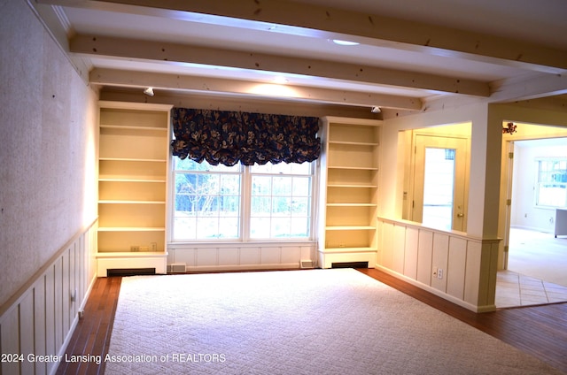 empty room with wood-type flooring, built in features, and beam ceiling