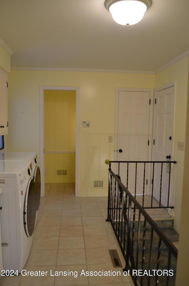 clothes washing area with light tile patterned flooring, washer / dryer, ornamental molding, and cabinets