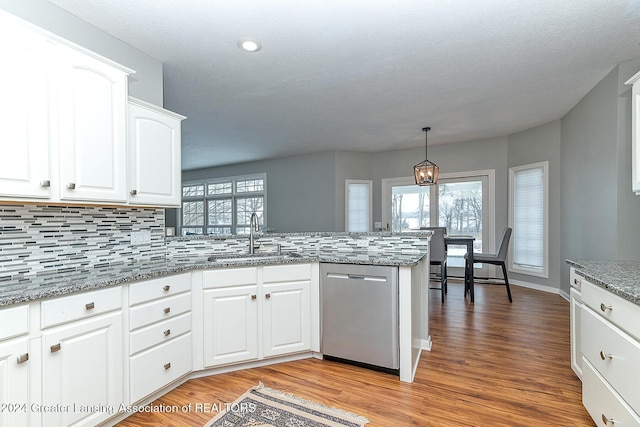 kitchen featuring pendant lighting, stainless steel dishwasher, kitchen peninsula, sink, and white cabinetry