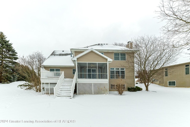 snow covered back of property featuring a wooden deck and a sunroom