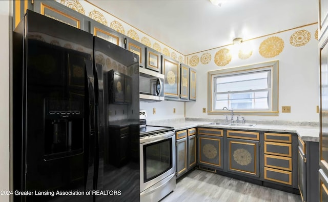 kitchen with light stone countertops, light wood-type flooring, stainless steel appliances, and sink