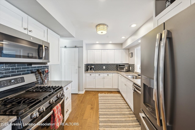 kitchen with light hardwood / wood-style flooring, decorative backsplash, light stone countertops, white cabinetry, and stainless steel appliances