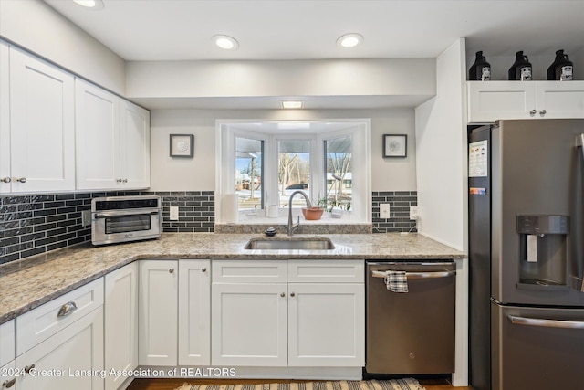 kitchen with appliances with stainless steel finishes, backsplash, light stone counters, sink, and white cabinets